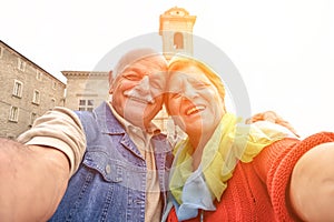 Senior couple taking a selfie in old town center - Two persons in the 60`s having fun with new technologies outdoor at sunset - photo