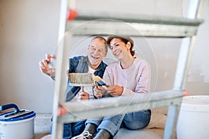 Senior couple taking selfie when painting walls in new home, relocation concept.