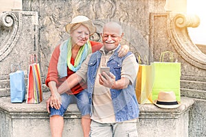 Senior couple taking selfie after shopping with smartphone - Happy tourist in the 60`s having fun with new technologies outdoor photo