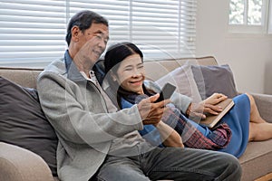 A senior couple in their 60s spends their free time relaxing and having fun together on the sofa in the living room.