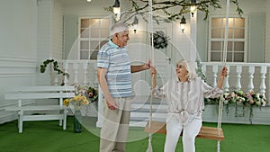 Senior couple together in front yard at home. Man swinging woman. Happy elderly pensioners family