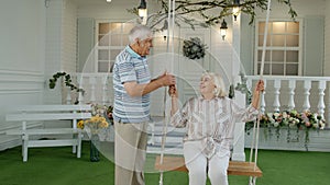 Senior couple together in front yard at home. Man swinging woman. Happy mature retired family