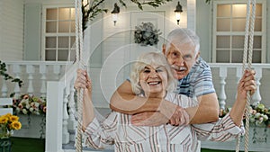 Senior couple together in front yard at home. Man swinging woman. Happy mature retired family