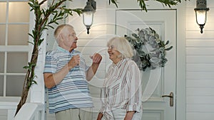 Senior couple together in porch at home. Mature man stands and his wife comes to embrace him