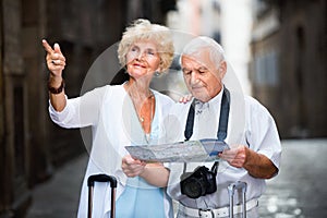 Senior couple of tourists with map and city guide walking
