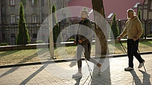 Senior couple with trekking poles walking in the street. Practicing scandinavian walking outdoors. Aging youthfully