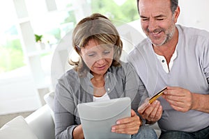 Senior couple using credit car doing online shopping