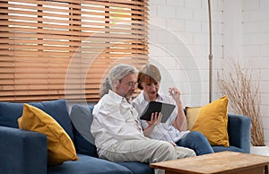 Senior couple using digital tablet while sitting on sofa in living room