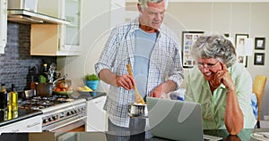 Senior couple using laptop while cooking in kitchen 4k