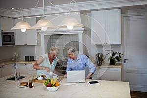 Senior couple using laptop while having tea in kitchen