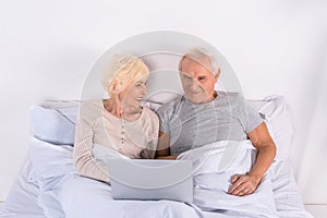 senior couple using laptop while resting in bed