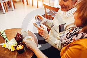 Senior couple using a phone in cafe. Retired people learn how to use new technolodies. Family relaxes in cafe