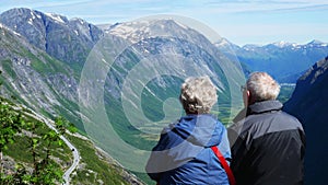 Senior couple on vacation in mountains. Mature man and woman enjoying the view of a green valley and mountains with snow.