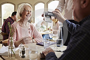 Senior Couple With Waiter Paying Bill In Restaurant