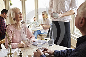 Senior Couple With Waiter Paying Bill In Restaurant
