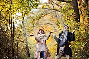 Senior couple on a walk in a forest in an autumn nature, throwing leaves.