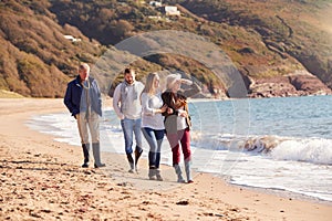 Senior Couple Walking Along Shoreline With Adult Offspring On Winter Beach Vacation