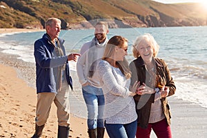 Senior Couple Walking Along Shoreline With Adult Offspring On Winter Beach Vacation