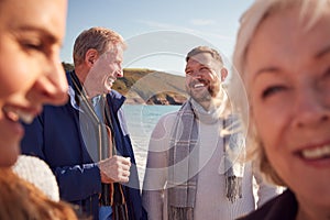 Senior Couple Walking Along Shoreline With Adult Offspring On Winter Beach Vacation