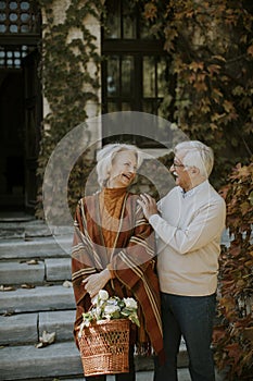 Senior couple walking with basket full of flowers and groceries in autumn park
