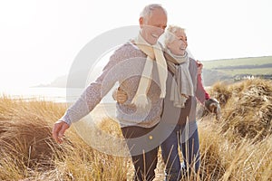 Senior Couple Walking Through Sand Dunes On Winter Beach