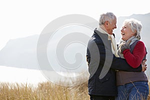 Senior Couple Walking Through Sand Dunes On Winter Beach