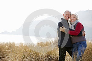 Senior Couple Walking Through Sand Dunes On Winter Beach