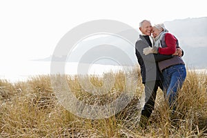 Senior Couple Walking Through Sand Dunes On Winter Beach