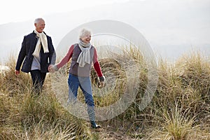 Senior Couple Walking Through Sand Dunes On Winter Beach