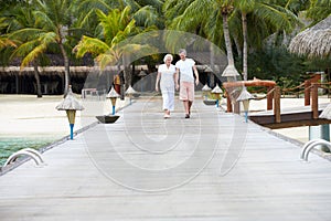 Senior Couple Walking On Wooden Jetty