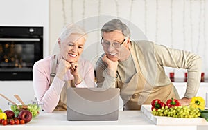 Senior Couple Watching Online Cooking Course On Laptop In Kitchen