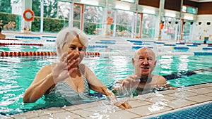 Senior couple waving to the camera in the swimming pool