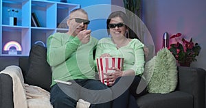 Senior couple Wearing 3d Glasses and eating popcorn. Older man and woman watching tv together, sitting at home on sofa