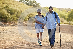 Senior Couple Wearing Backpacks Hiking In Countryside Together