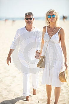 senior couple wearing white clothes walking on beach