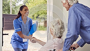 Senior Couple With Woman In Wheelchair Greeting Nurse Or Care Worker Making Home Visit At Door