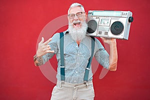 Senior crazy man with 80`s boombox stereo playing rock music with red background - Trendy mature guy having fun dancing with