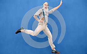 Senior crazy man jumping while listening music with wireless headphones - Hipster old guy having fun dancing outdoor