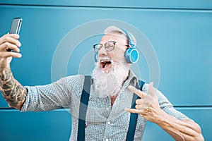 Senior crazy man taking self video while listening music with headphones - Hipster guy having fun using mobile smartphone