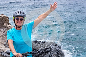 Senior cyclist woman in outdoor sea excursion happily greets. Active lifestyle during retirement