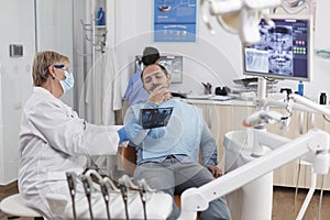 Senior dentist woman with face mask explaining teeth radiography