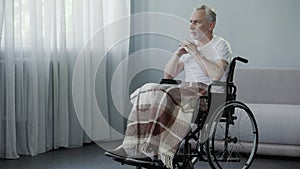 Senior disabled man sitting in wheelchair and looking in window, waiting family