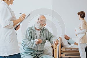 Senior doctor in a beige uniform talks to an elderly patient during a walk around hospital photo