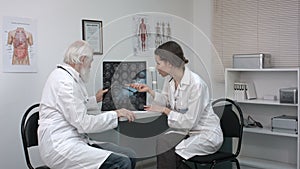 Senior doctor examines MRI image of human head. Senior man doctor teaches young woman doctor.