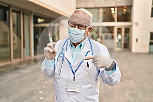 Senior doctor with grey hair wearing safety mask holding syringe pointing finger to one self smiling happy and proud