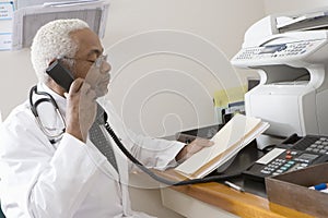 Senior Doctor Holding Document While Using Landline Phone photo