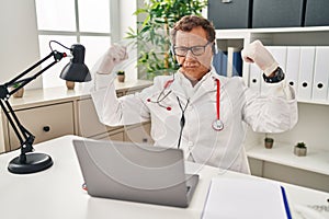 Senior doctor man working on online appointment showing arms muscles smiling proud