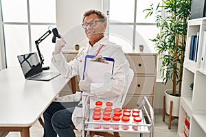 Senior doctor man working with samples pointing thumb up to the side smiling happy with open mouth