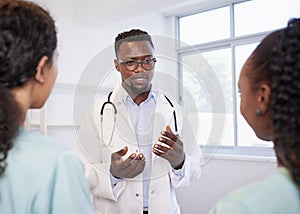 Senior doctor talks to junior healthcare assistants, standing team in hospital photo
