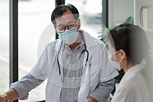 Senior doctor wearing safety protective mask supporting and cheering up young patient during home visit during virus and